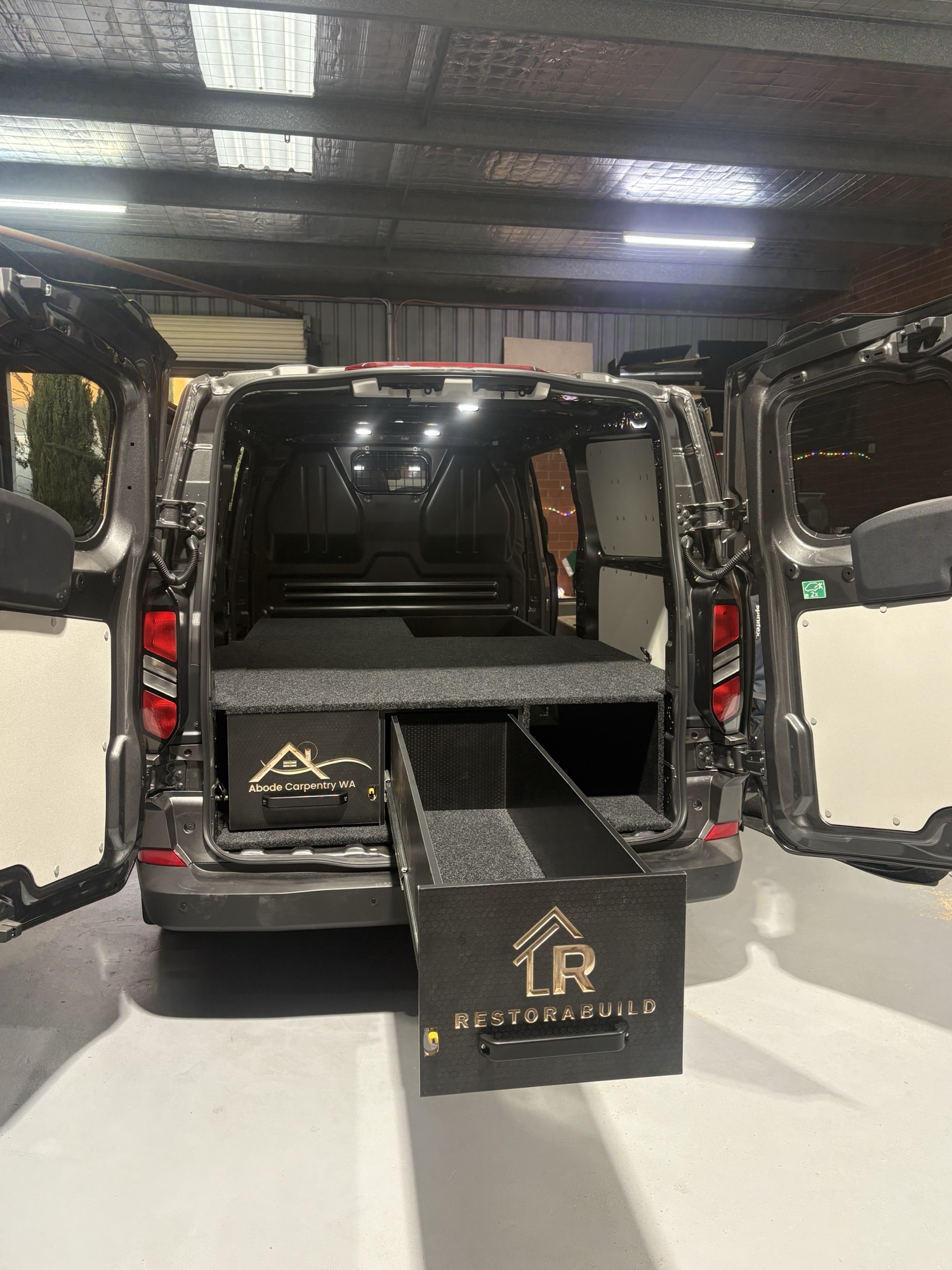 Black tradie van in the Bandit workshop, both rear doors open, Restorabuild drawer slid out